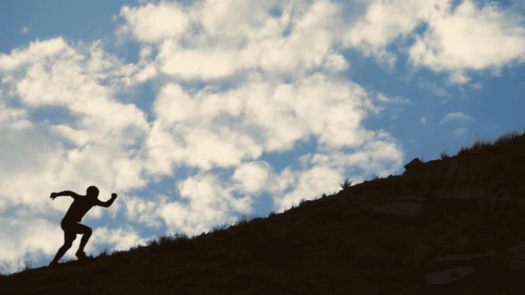 man running up  hill with clouds behind